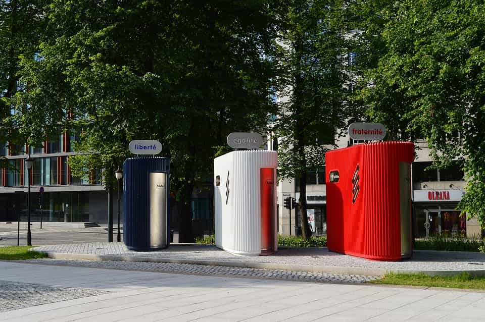 Toilettes publiques de type sanisette dans un parc, peintes en bleu, blanc et rouge.